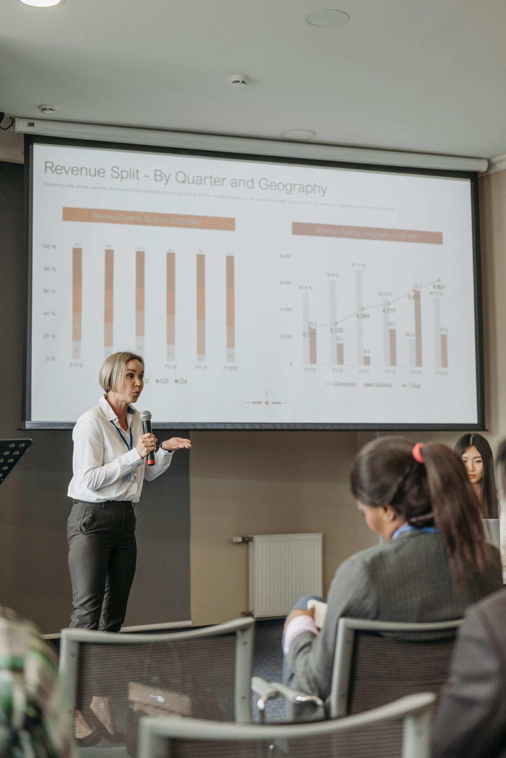 A professional woman leads a seminar on revenue analysis, engaging participants with graphs and data.